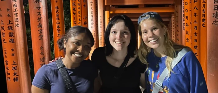 Three women stand in front of the vermillion gates of Fushimi Inari Shrine