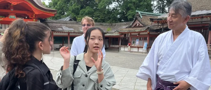 A student interpreter gestures while speaking with a Kyoto Project student and a Shinto priest in the courtyard of a shrine in Kyoto.