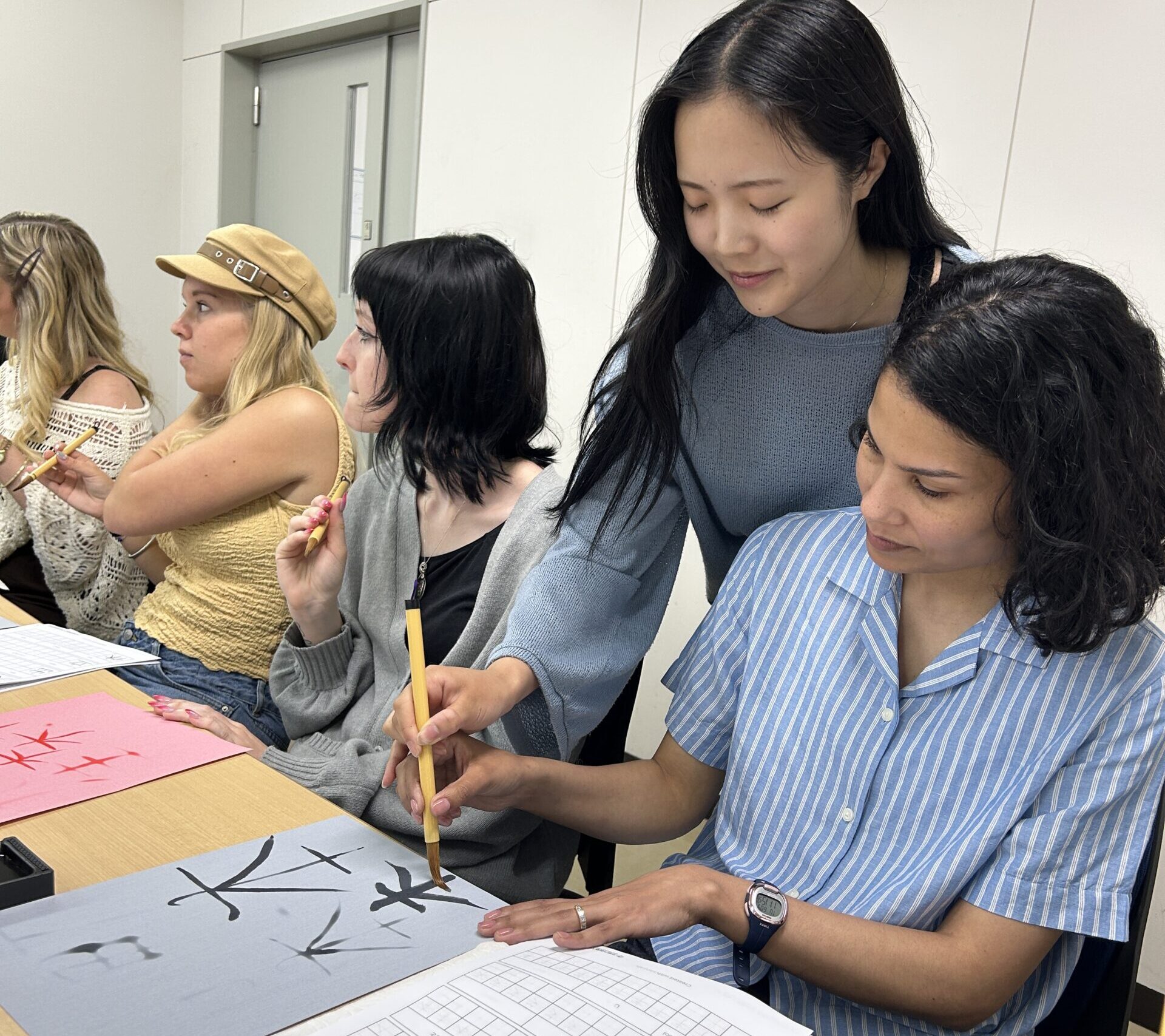 A Japanese student guides an American student in calligraphy.