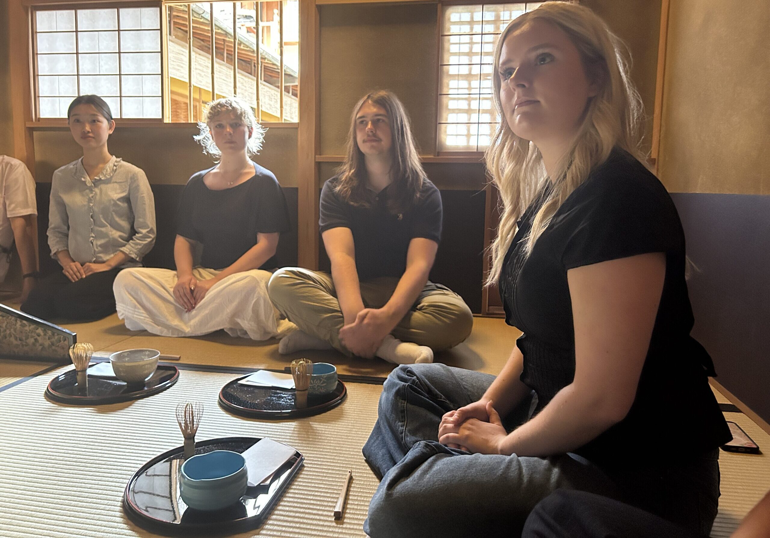 Young people sit on the floor of a traditional Japanese tea room with tatami mats